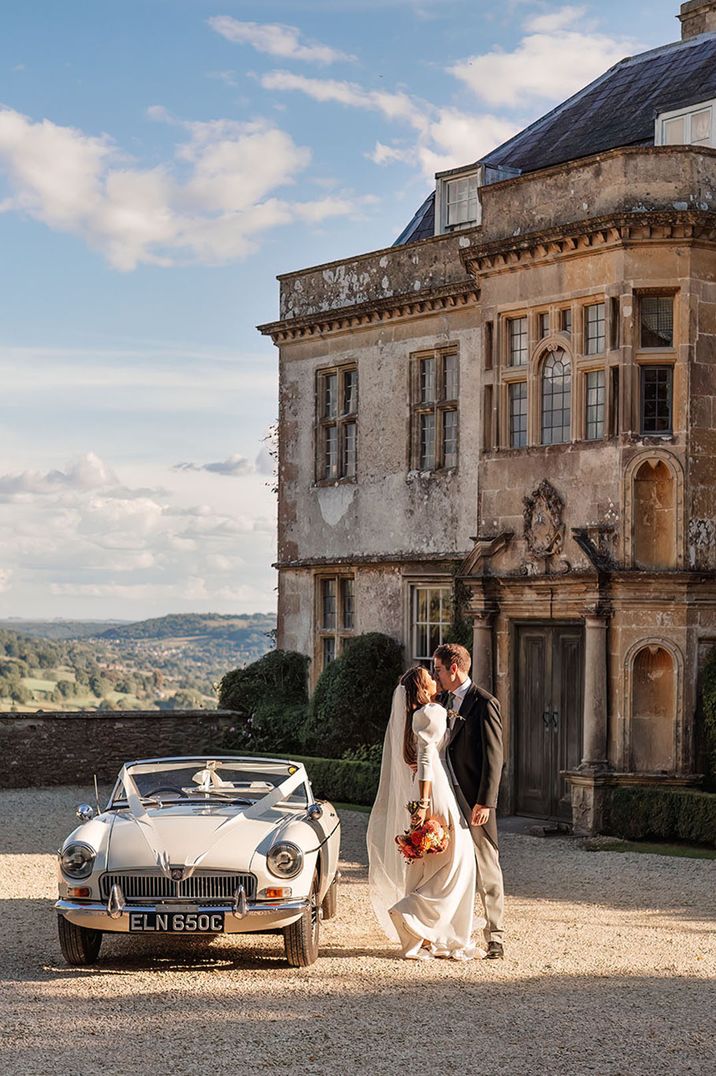 Hamswell House wedding venue with classic cream vintage wedding car decorated with white ribbon 