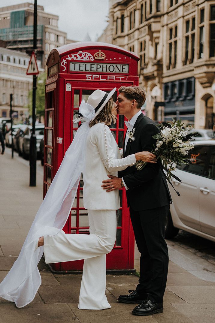 Bride wears white bridal hat with veil and Nadine Merabi wedding suit 