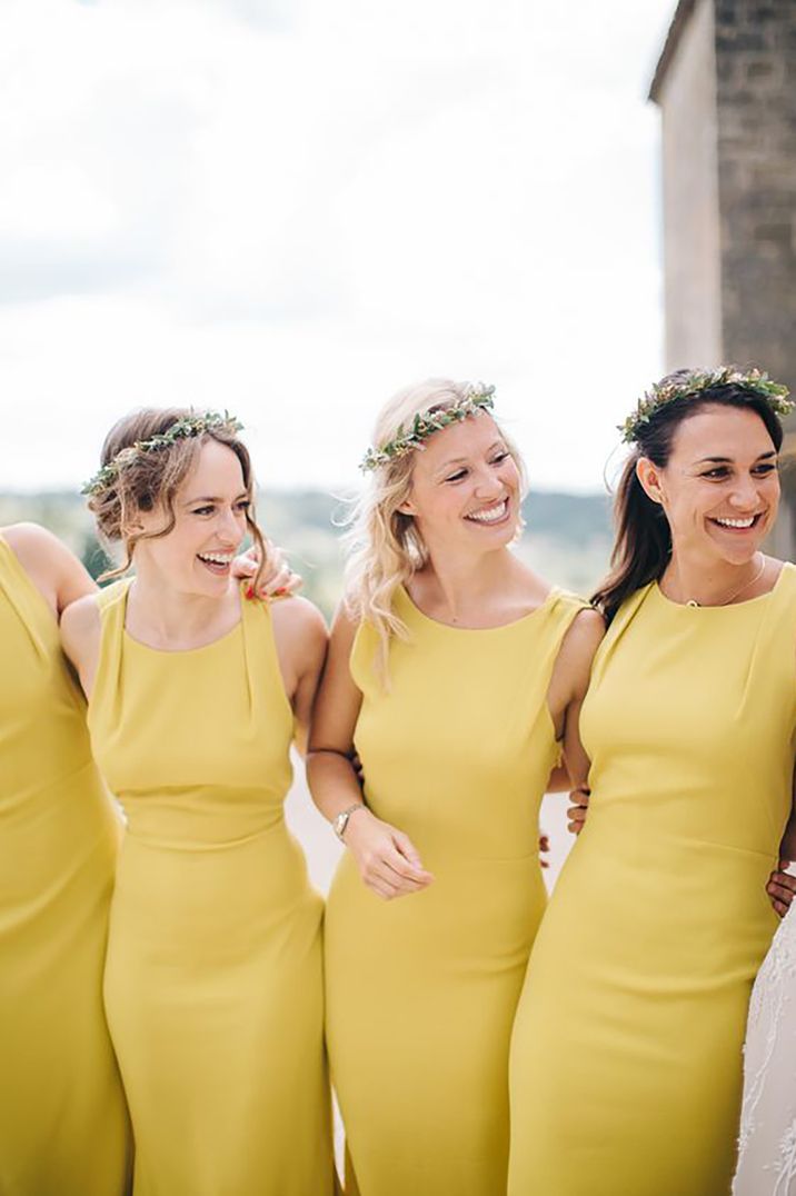 Four bridesmaids standing arm in arm smiling wearing yellow bridesmaid dresses by M&J Photography