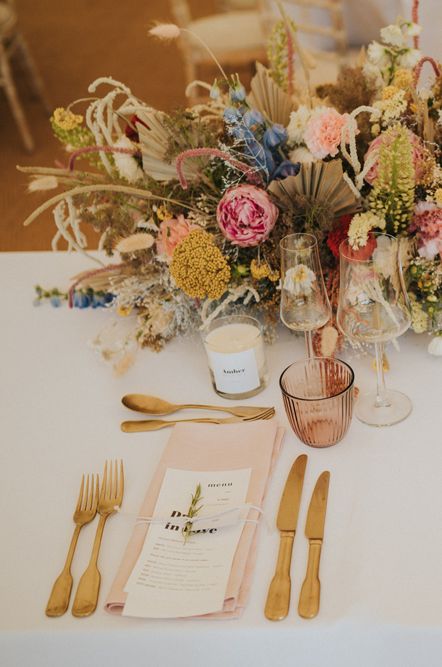 Marquee reception place setting with gold cutlery, pink napkins, and a top table flower arrangement with dried palm leaves and anthuriums 