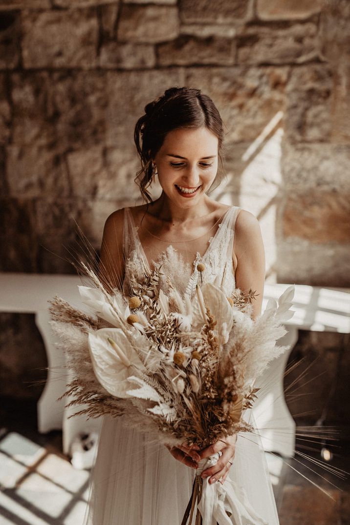 Beautiful bride holding a dried and fresh flower wedding bouquet with white anthuriums, billy bobs and pampas grass