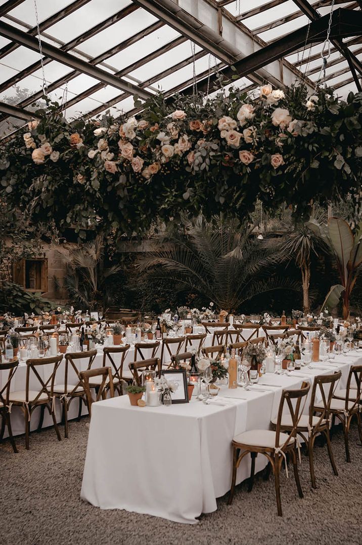 Anran glasshouse wedding venue with long banquet tables with white tablecloth simple table decor and large flower installation 