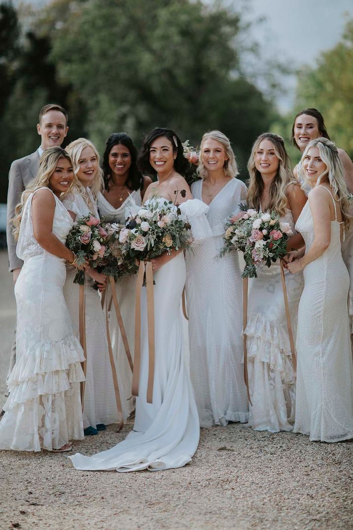 Bride in off the shoulder wedding dress standing with wedding party with bridesmaids in sleeveless layered white bridesmaid dresses 