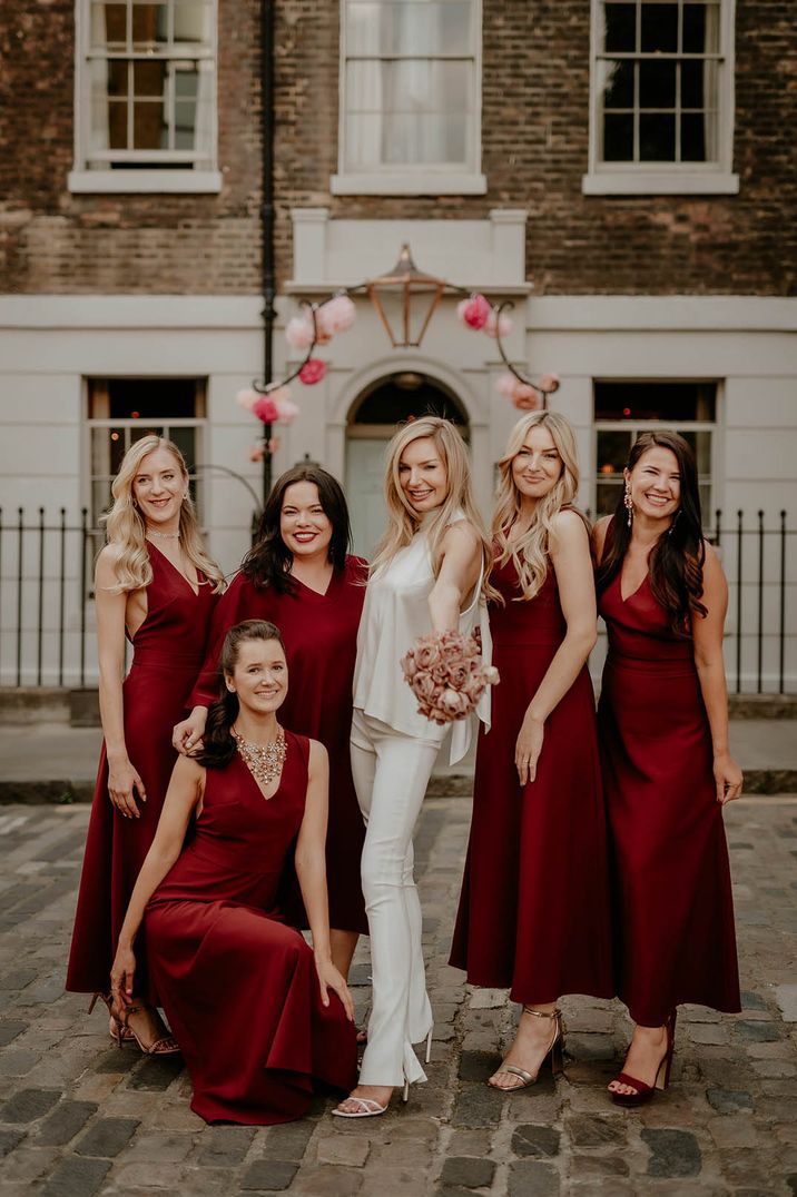 Bride in sleek bridal suit with bridal party in mismatched burgundy bridesmaid dresses at The Zetter Townhouse 