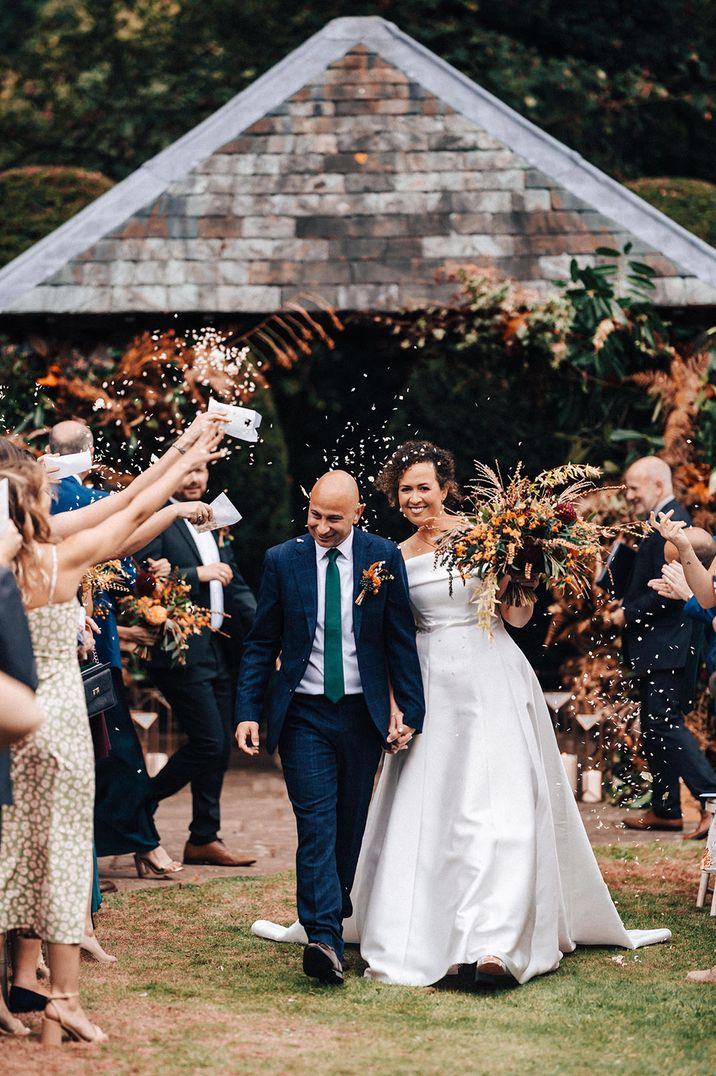 Confetti moment at outdoor wedding with the bride carrying an autumnal orange wedding bouquet 