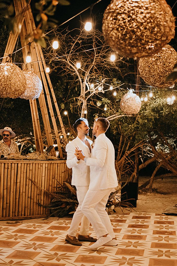 Two grooms in white suits share their first dance together at their destination wedding 