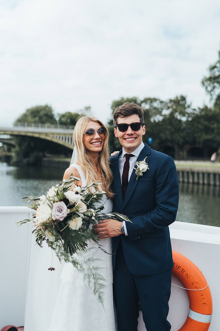 Bride in strappy wedding dress with long veil, groom in dark blue suit on their boat wedding transport