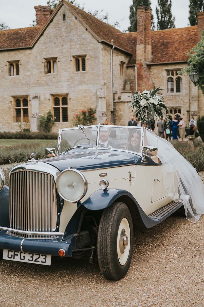 Bride and groom at Notley Abbey in a classic convertible deep blue wedding car with cream stripes