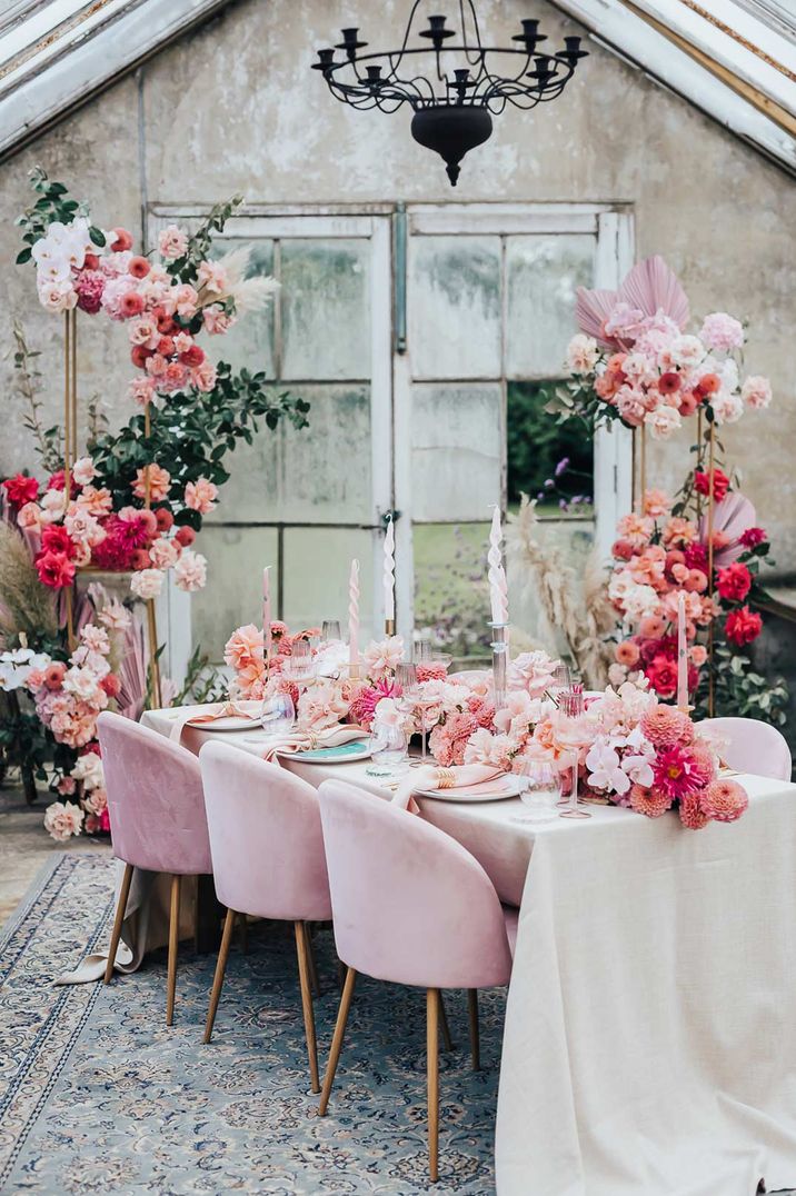 Opulent pink wedding tablescape with pink velvet chairs, large pink floral arrangements, pink twisted tapered candles and large black chandelier 