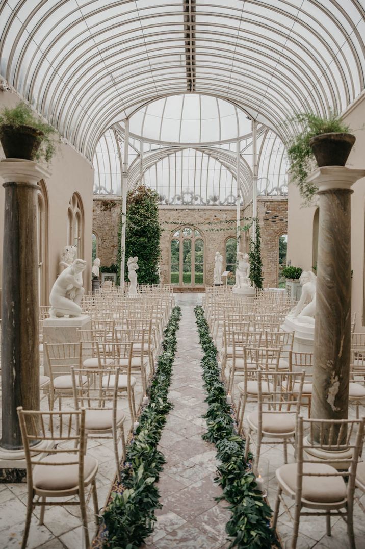 All white glasshouse wedding venue in Ireland with green aisle decoration with statues 