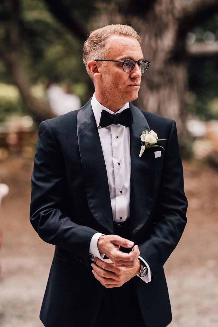 Groom in velvet tuxedo with round framed glasses and boutonnière 