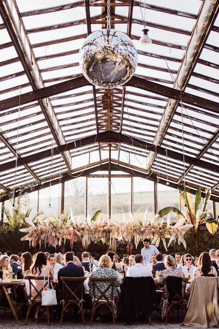 Large disco ball wedding decor and suspended pampas grass and foliage decor at Devon glasshouse wedding venue 