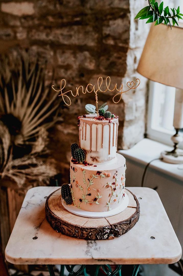 Two tiered buttercream wedding cake with icing drip decor, icing roses, cactus decor and golden laser cut wedding cake topper 