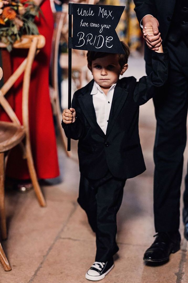 Page boy walking down the aisle with a groomsman with a funny sign 