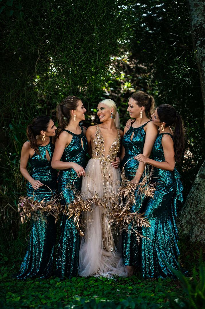 Bridal party portrait with bridesmaid in green sequin dresses holding hoop bouquets and bride in a gold wedding dress with sleek ponytail and green eyeshadow 