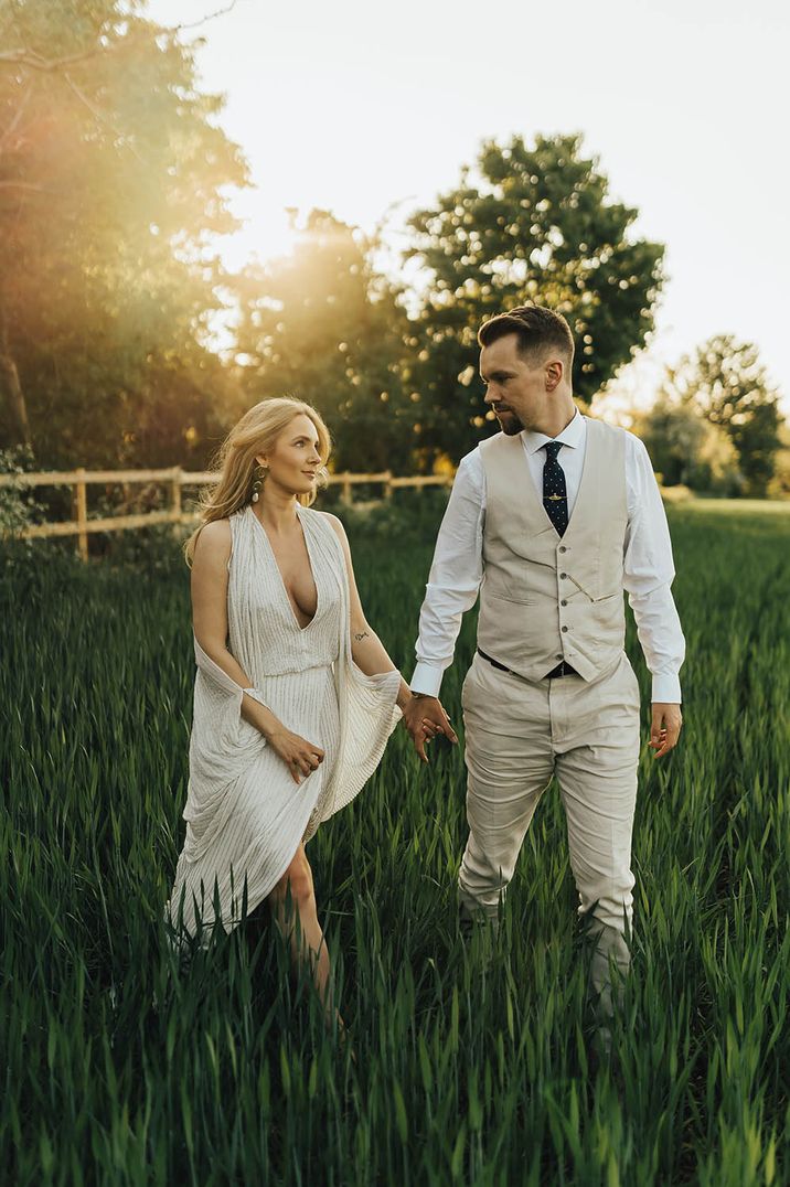 Golden hour portrait in a field with bride in a draped wedding dress with plunging neckline and groom in a beige suit 