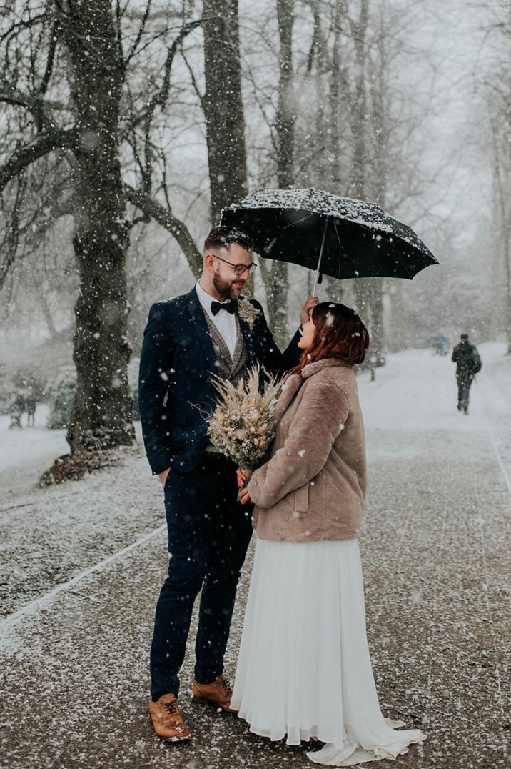 Bride and groom stand closely together for their snowy winter wedding 