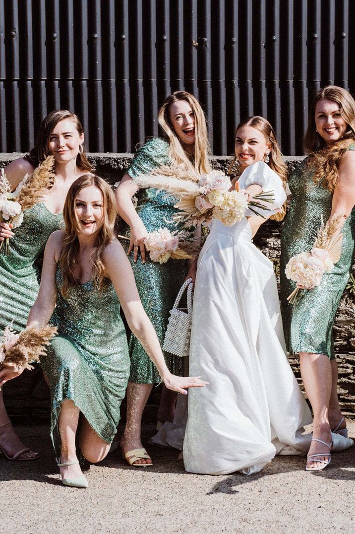 Bridesmaids in matching green sequin bridesmaid dresses smiling with the bride on the wedding day 