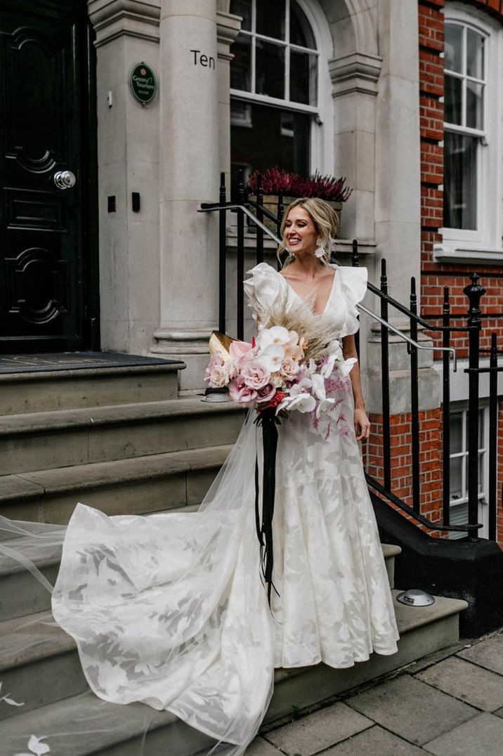 Bride in a Jesus Peiro ruffle wedding dress with pink tropical wedding bouquet tied with black ribbon 