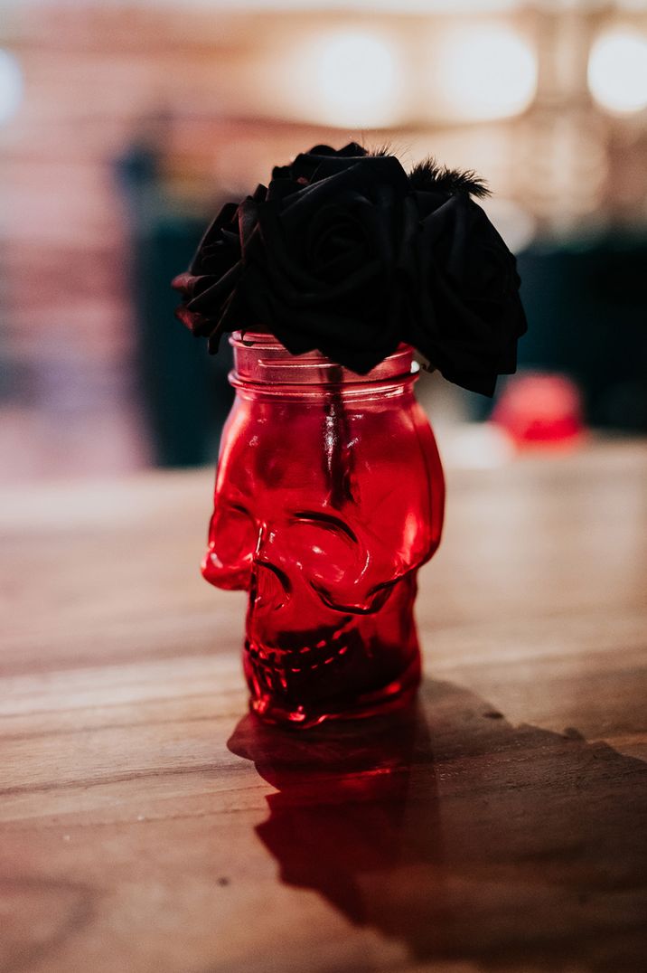 Red skull shaped vase full of black wedding flowers for table decoration 