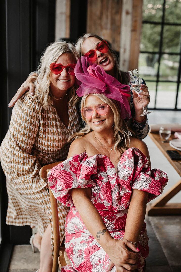 Three wedding guests posing for photo with one wearing a hot pink wedding fascinator and matching dress 