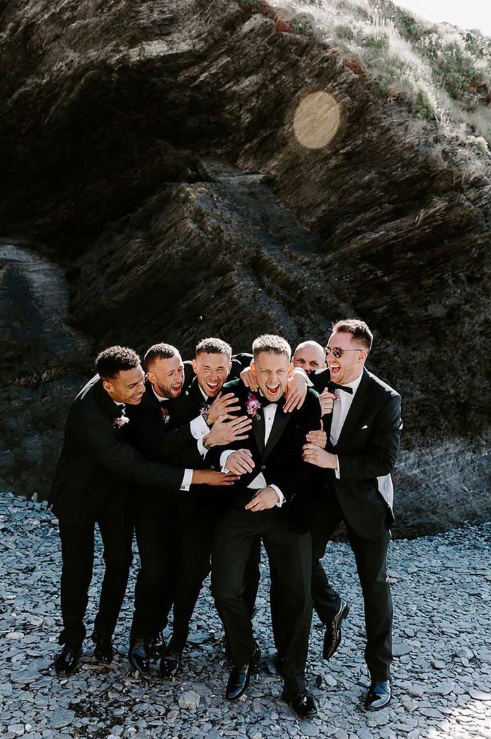 The groom and groomsmen wearing black tuxedos for beach wedding celebrating together 