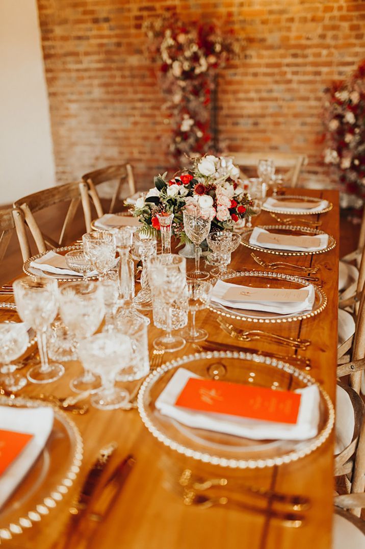 Clear charger plates with orange menu stationery and gold cutlery for rustic wedding tablescape