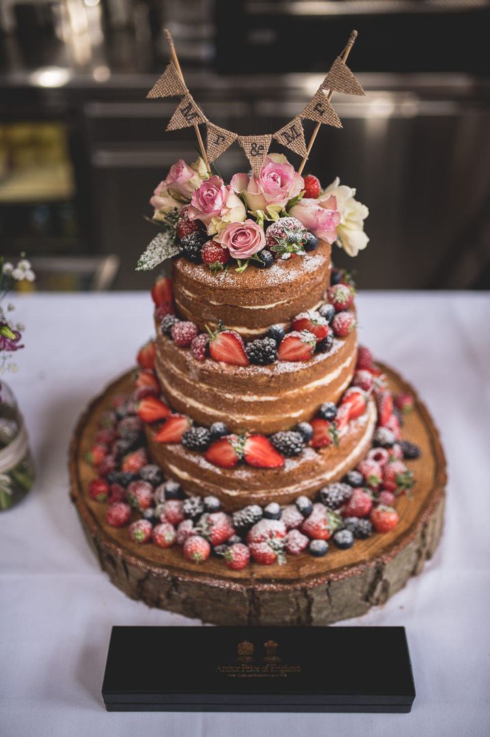 Naked wedding cake decorated with berries and a rustic bunting wedding cake topper 