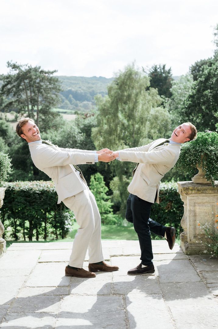 Groom and best man in light suits holding hands