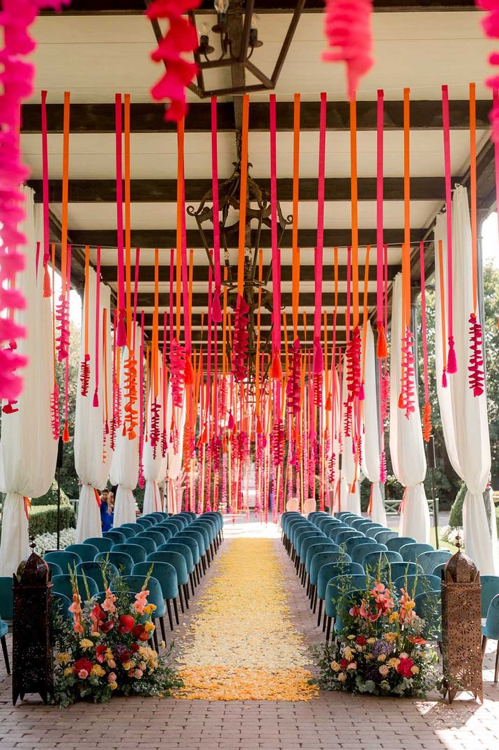 Wedding ceremony decor with hot pink and orange streamers hanging from the ceiling and flowers lining the aisle