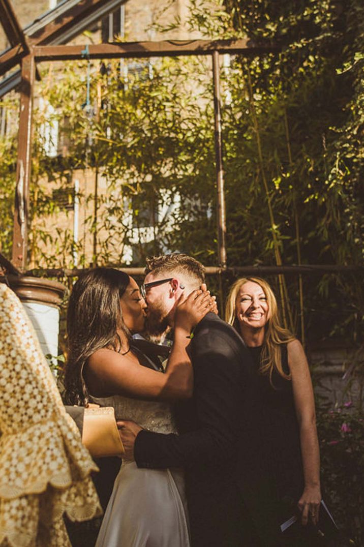 Bride in sleeveless wedding dress and groom in dark suit kissing at Clifton Nurseries London glass house wedding venues 