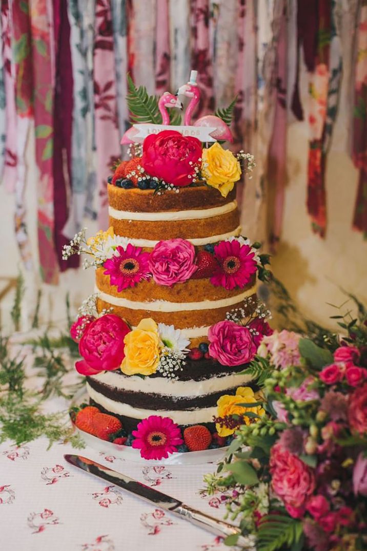 Naked wedding cake with bright and colourful pink and yellow flowers with flamingo cake toppers 