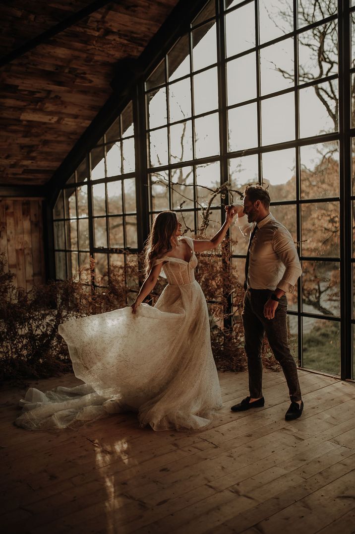 Groom spins the bride around at Hidden River Cabins wedding venue with large windows 