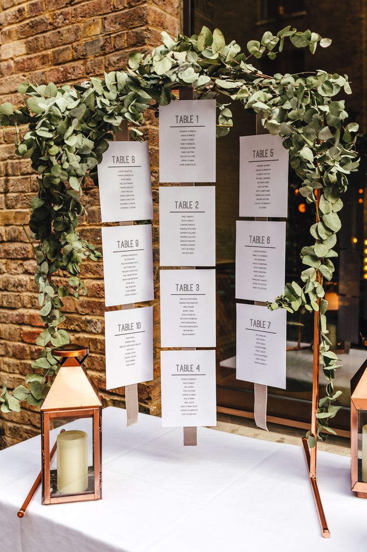 Hanging table plan on a copper frame with green leaves and candle lanterns 