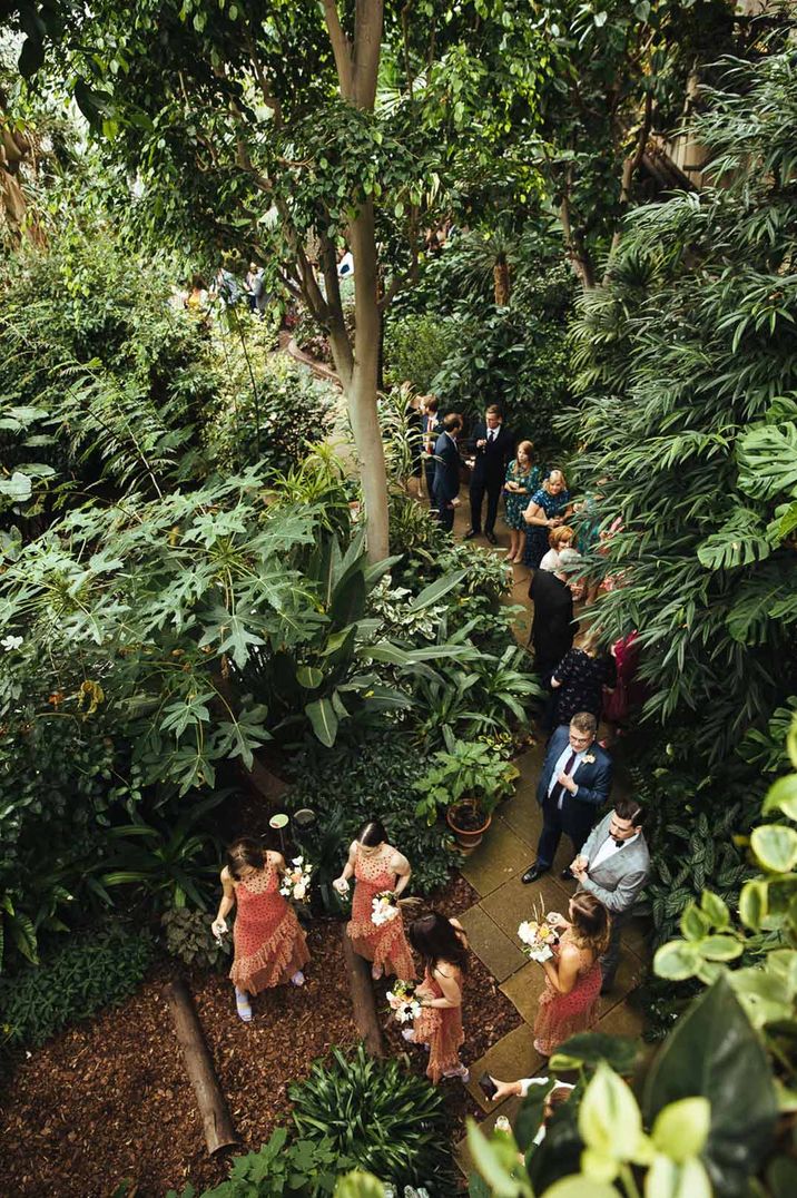 Guests in fringed orange bridesmaid dresses walking through The Barbican Conservatory glass house wedding venues 