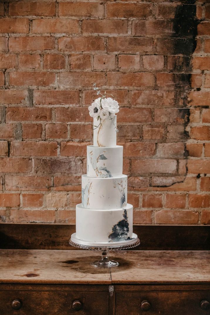 Epic four tier white iced wedding cake with gold flakes and geode pattern with white flower cake topper decor 