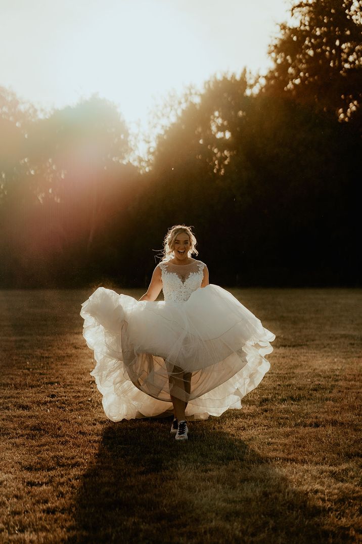 Bride in illusion style princess tulle wedding dress running in trainers at country house wedding 