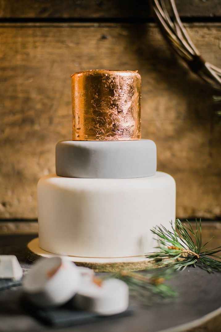 Three tier wedding cake with a white iced layer, grey iced layer and shiny gold layer 