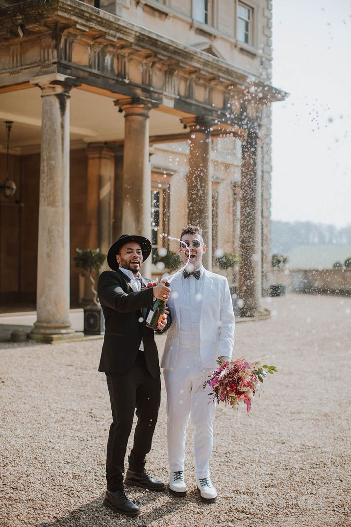 Two grooms pop champagne together as they celebrate their wedding 