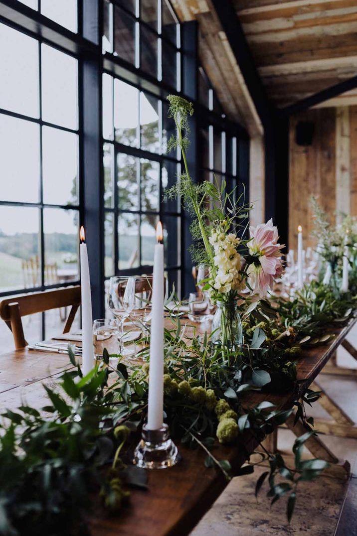 Wedding tables decorated with white taper candles and natural foliage decor 