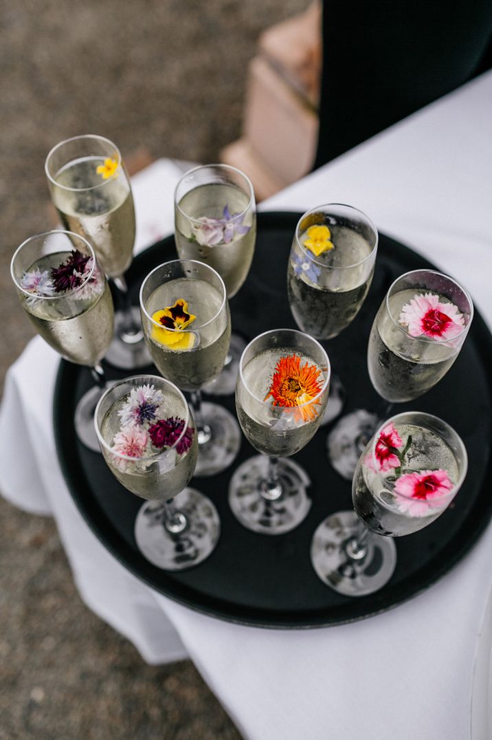 Glasses of champagne on black serving tray decorated with edible flowers 