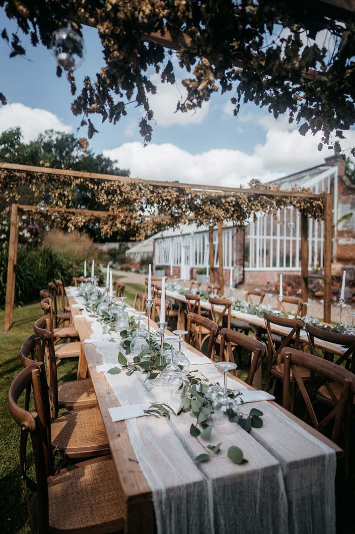 Neutral earthy outdoor wedding tablescape with sheer table runners, green foliage decor and large candle holders