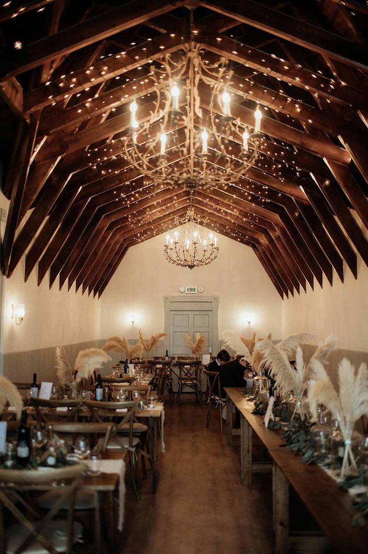 Reception room of The Dougarie Boathouse wedding venues Scotland with fairy lights, large chandeliers and pampas grass table centrepieces 