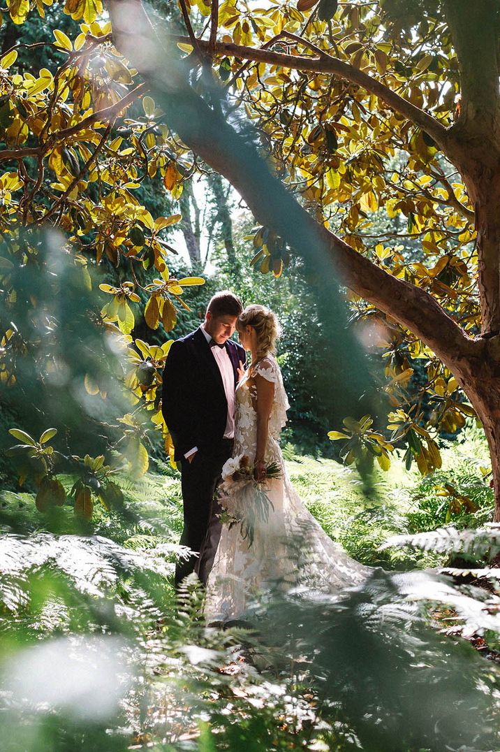 Cute couple portrait with from in black tuxedo posing with the bride in a floral lace gown  