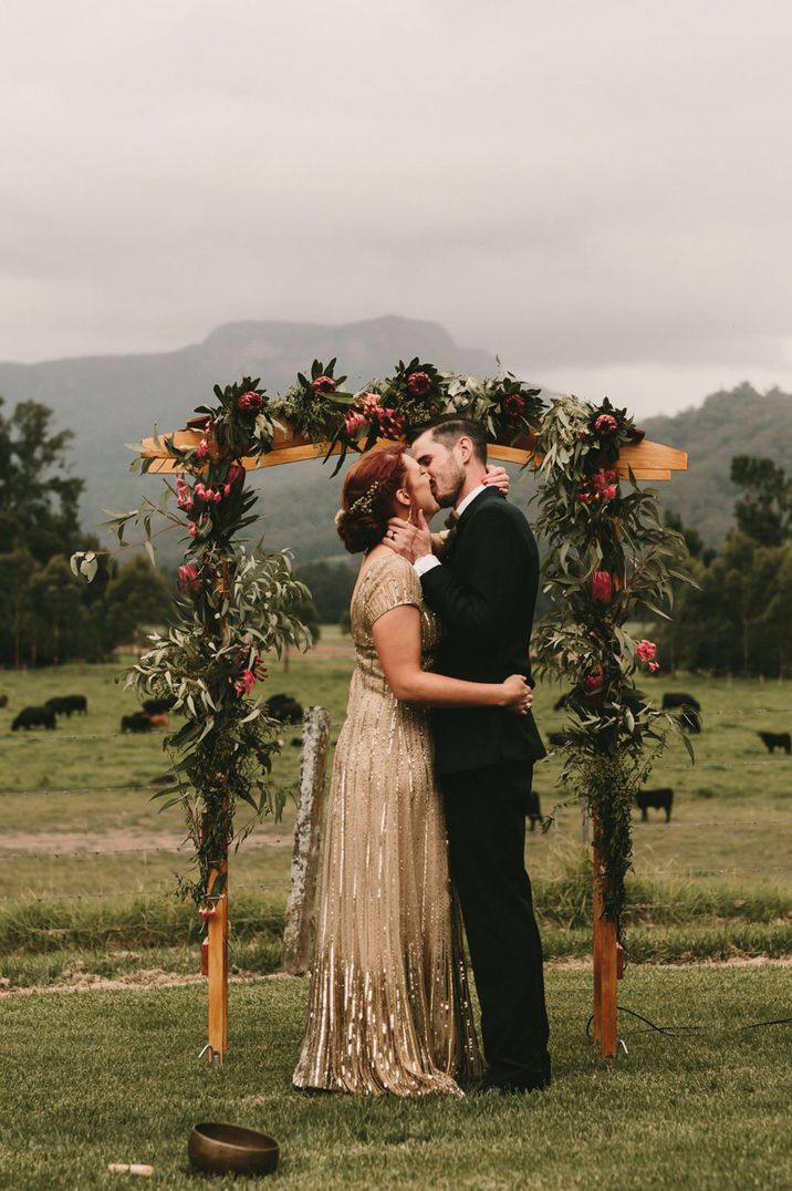 bride wearing gold coloured wedding dress kissing groom at altar