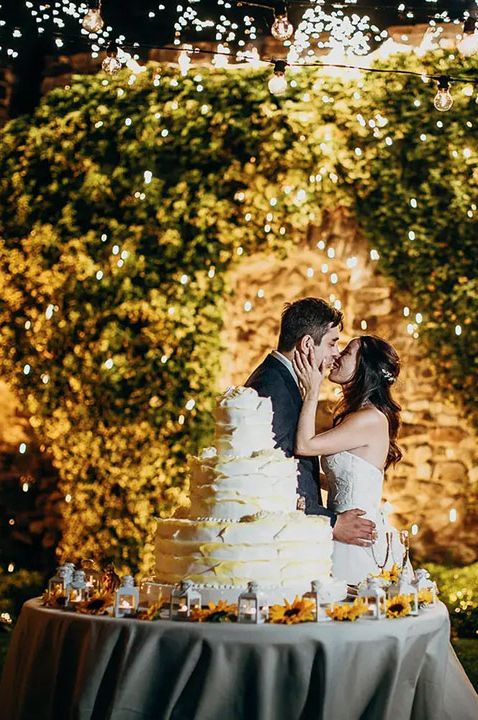 Castello di Rossino wedding venue in Italy - couple kissing by wedding cake and fairy light adorned wall 