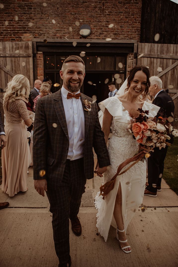 Groom walks out of the wedding with the bride as the guests throw confetti in celebration 