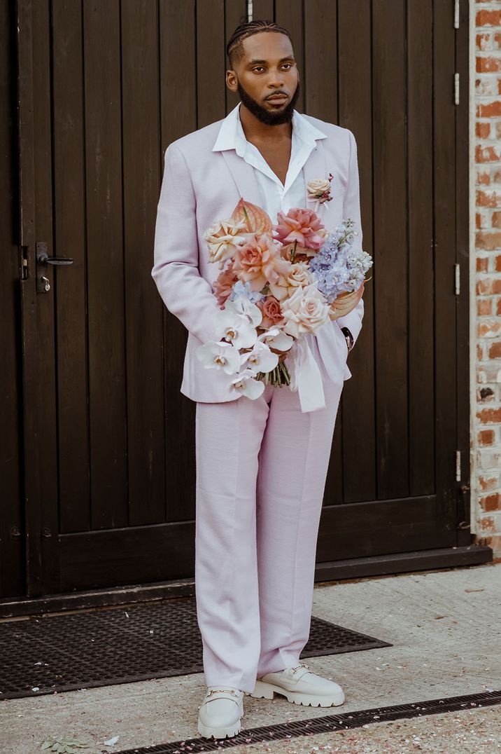 Groom in pale pink lilac wedding suit holding a pastel wedding bouquet for wedding 