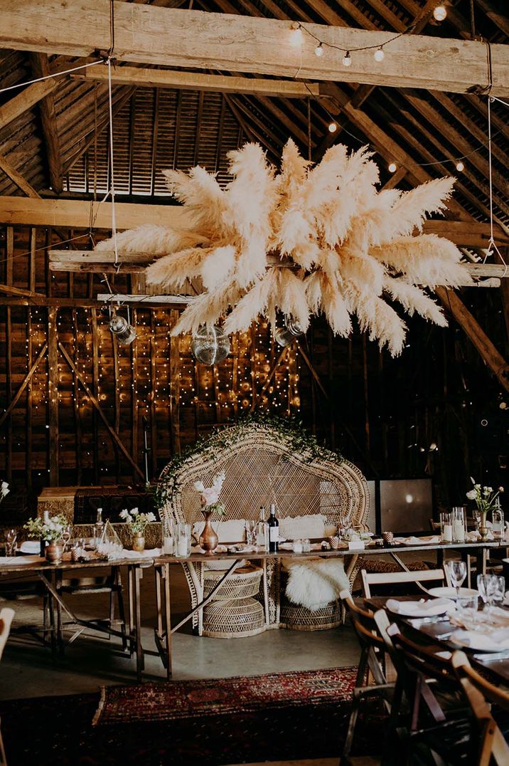 Large pampas grass cloud installation for boho wedding reception with fairy lights and peacock chairs