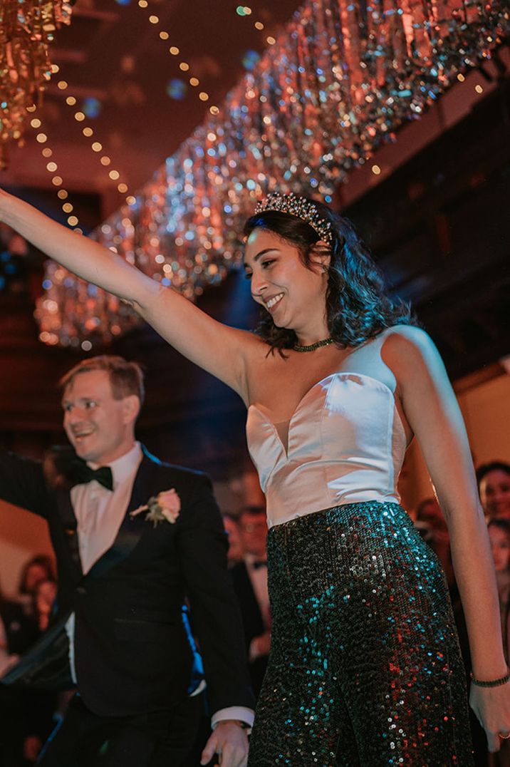 The bride wears a white satin crop top and dark green sequin trousers for her wedding reception outfit with pearl crown 